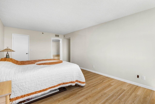 bedroom with light wood-style floors, a textured ceiling, and baseboards