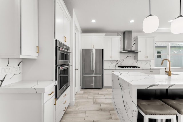 kitchen featuring a kitchen bar, appliances with stainless steel finishes, white cabinets, a sink, and wall chimney exhaust hood