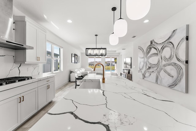 kitchen featuring tasteful backsplash, a wealth of natural light, hanging light fixtures, gas cooktop, and wall chimney exhaust hood