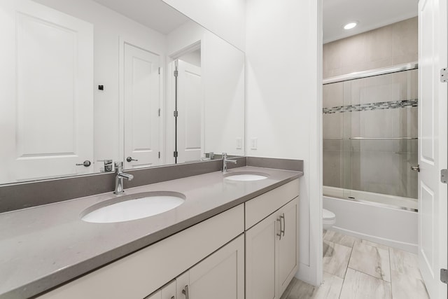 bathroom with toilet, shower / bath combination with glass door, double vanity, and a sink