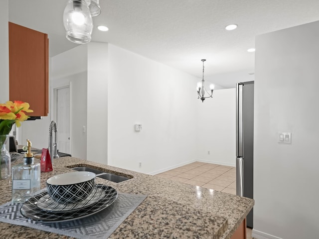 kitchen featuring light tile patterned floors, light stone counters, recessed lighting, a sink, and decorative light fixtures