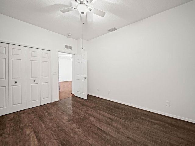 unfurnished bedroom featuring dark wood-style floors, a textured ceiling, visible vents, and a closet