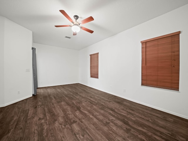 empty room with a ceiling fan, visible vents, dark wood finished floors, and baseboards