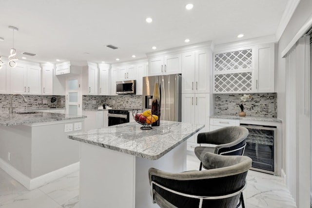 kitchen with beverage cooler, visible vents, a kitchen island, stainless steel appliances, and a sink