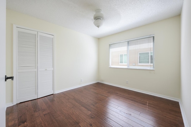 unfurnished bedroom featuring a textured ceiling, dark wood-type flooring, a closet, and baseboards