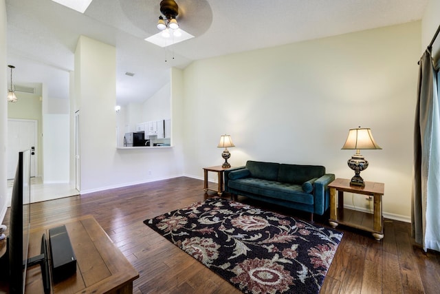 living room featuring lofted ceiling with skylight, wood-type flooring, baseboards, and ceiling fan