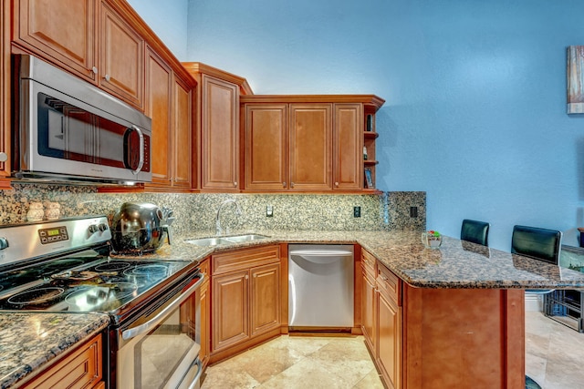 kitchen with a peninsula, a sink, dark stone counters, backsplash, and appliances with stainless steel finishes