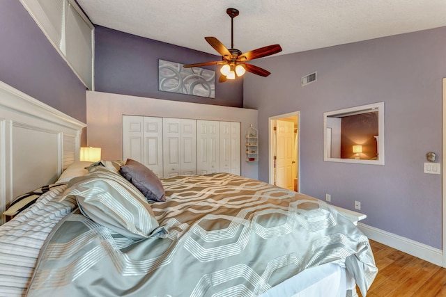 bedroom featuring a closet, light wood-style flooring, baseboards, visible vents, and high vaulted ceiling