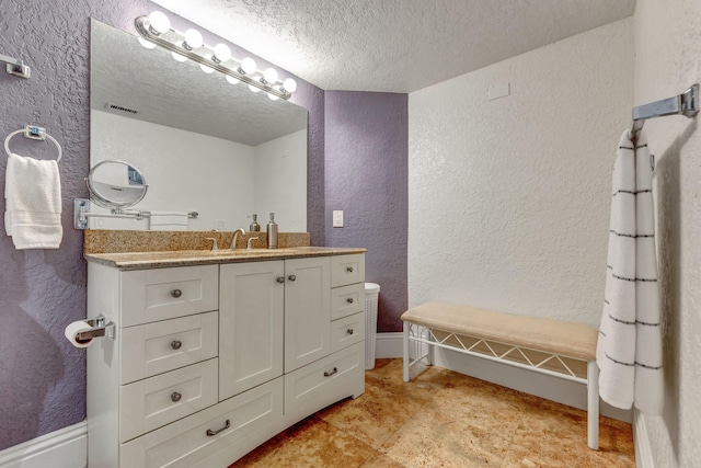 bathroom featuring a textured ceiling, baseboards, visible vents, vanity, and a textured wall