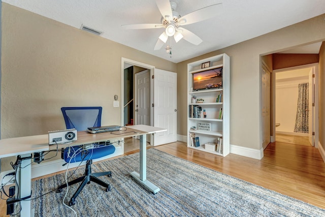 home office with baseboards, visible vents, ceiling fan, and wood finished floors