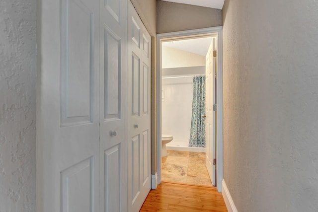 hall featuring lofted ceiling, a textured wall, and light wood finished floors