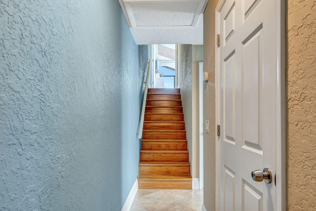 stairway featuring baseboards, attic access, and a textured wall