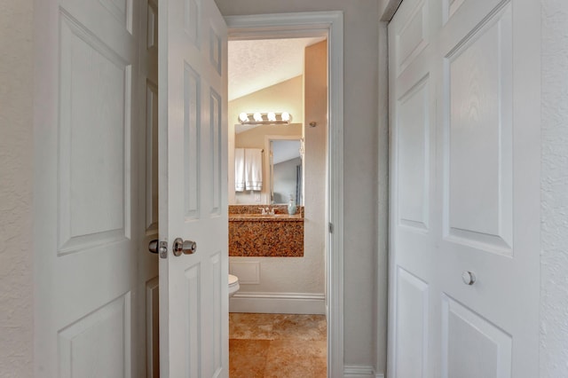 half bathroom featuring toilet, vaulted ceiling, a textured ceiling, and a textured wall