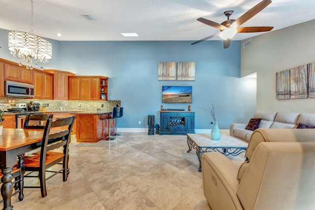 living room featuring a high ceiling, visible vents, baseboards, and ceiling fan with notable chandelier