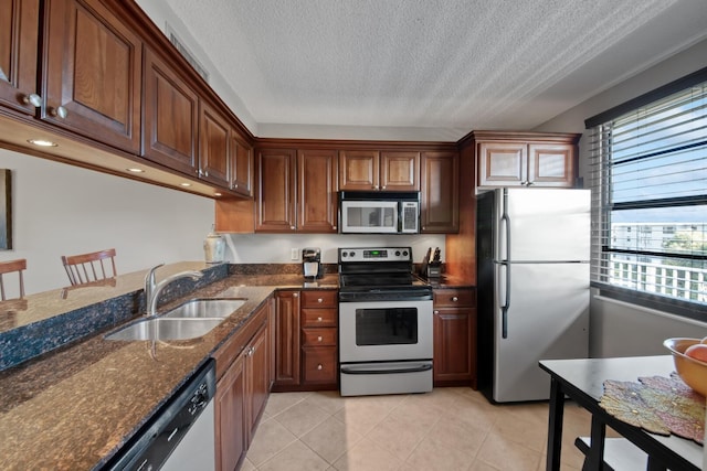 kitchen featuring light tile patterned floors, dark stone countertops, appliances with stainless steel finishes, a textured ceiling, and a sink