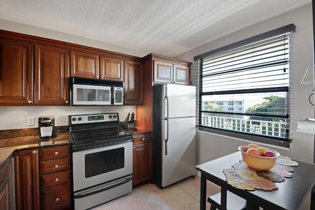 kitchen with light tile patterned floors, dark stone counters, a textured ceiling, and appliances with stainless steel finishes