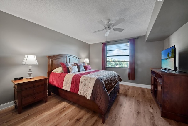 bedroom with ceiling fan, baseboards, light wood finished floors, and a textured ceiling