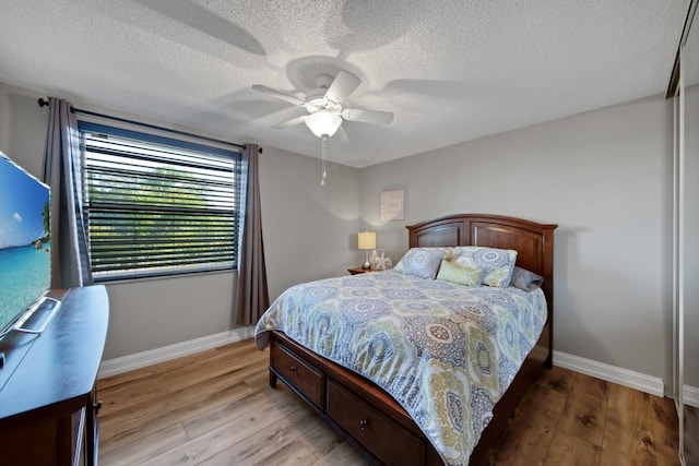 bedroom with ceiling fan, baseboards, light wood-type flooring, and a textured ceiling