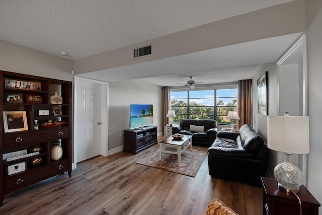 living area with visible vents, ceiling fan, baseboards, wood finished floors, and a textured ceiling