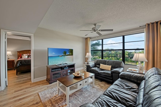 living room with light wood-style flooring, a ceiling fan, baseboards, and a textured ceiling