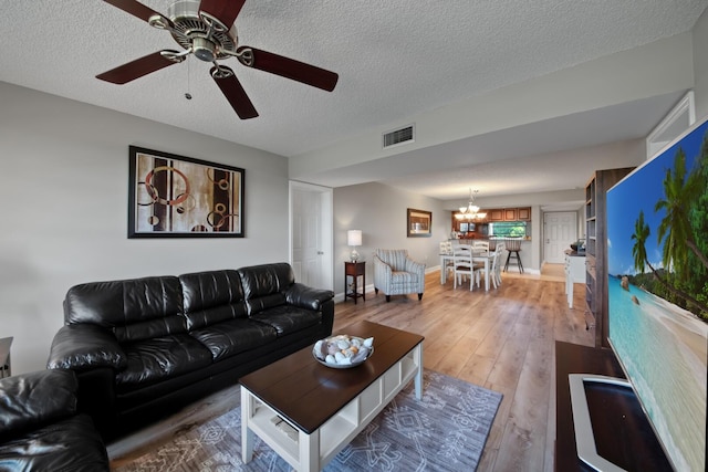 living room with baseboards, visible vents, a textured ceiling, and light wood-style floors