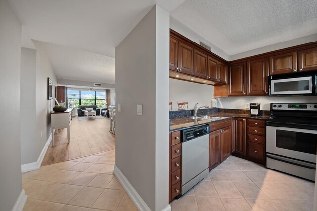 kitchen with dark stone counters, light tile patterned floors, appliances with stainless steel finishes, a textured ceiling, and a sink