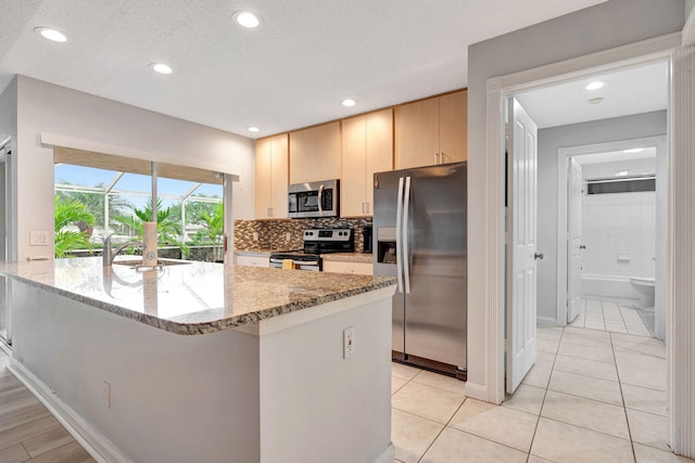 kitchen featuring decorative backsplash, light stone counters, stainless steel appliances, light brown cabinetry, and a sink