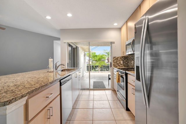 kitchen with light tile patterned floors, light brown cabinets, stainless steel appliances, a sink, and decorative backsplash