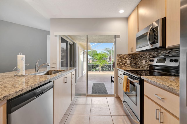 kitchen with light tile patterned floors, a sink, appliances with stainless steel finishes, light stone countertops, and tasteful backsplash