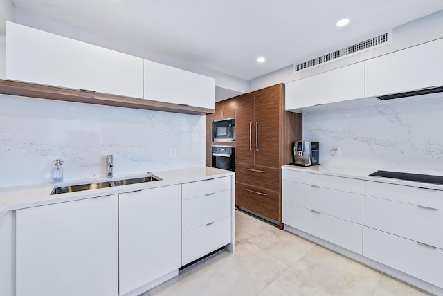 kitchen featuring visible vents, decorative backsplash, modern cabinets, black appliances, and a sink