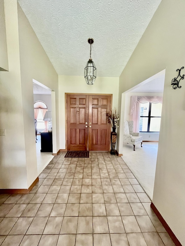 entryway featuring an inviting chandelier, baseboards, a textured ceiling, and light tile patterned flooring