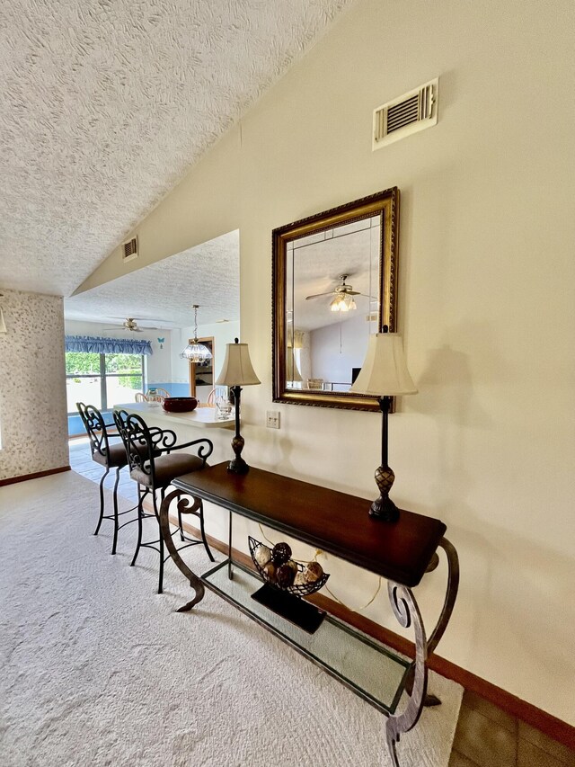 hallway with lofted ceiling, a textured ceiling, carpet flooring, and visible vents