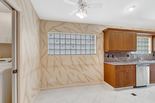 kitchen with light stone countertops, a sink, stainless steel dishwasher, brown cabinets, and washer / clothes dryer