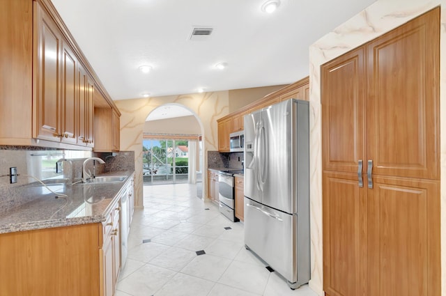 kitchen with stone countertops, stainless steel appliances, a sink, visible vents, and decorative backsplash