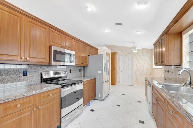 kitchen with visible vents, a ceiling fan, light stone counters, stainless steel appliances, and a sink