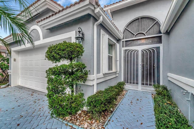 view of exterior entry featuring a garage, a tiled roof, decorative driveway, and stucco siding