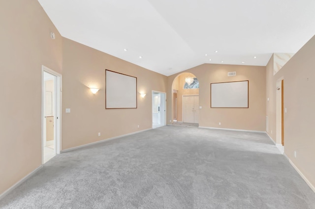 unfurnished living room with arched walkways, high vaulted ceiling, light colored carpet, and baseboards