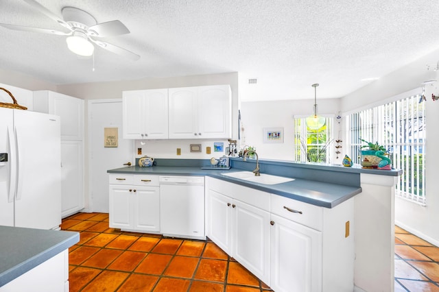 kitchen with dark countertops, white cabinets, a sink, white appliances, and a peninsula