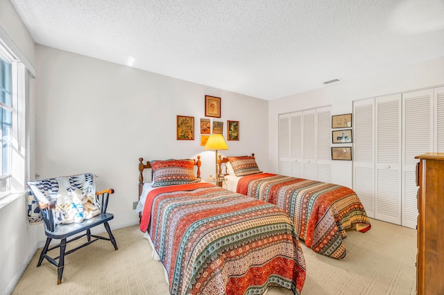 carpeted bedroom featuring a textured ceiling, two closets, and visible vents