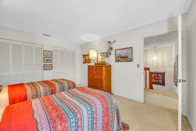 bedroom featuring visible vents, a textured ceiling, light colored carpet, and multiple closets