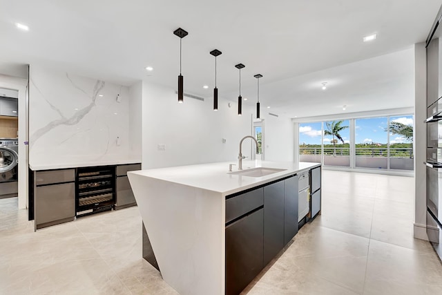 kitchen featuring a sink, hanging light fixtures, washer / clothes dryer, modern cabinets, and a center island with sink