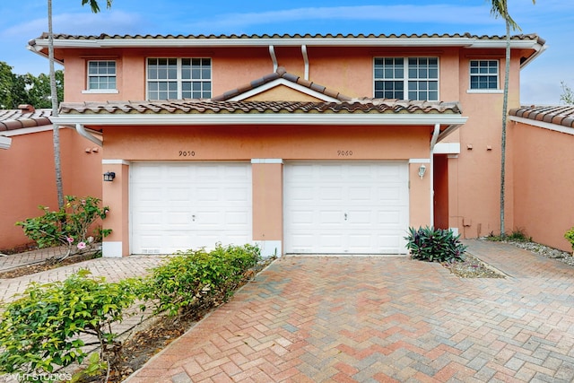 view of property with an attached garage, decorative driveway, and stucco siding