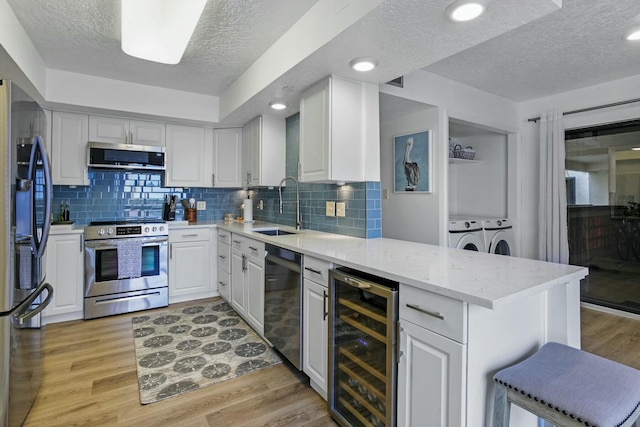 kitchen featuring wine cooler, independent washer and dryer, stainless steel appliances, light wood-type flooring, and a sink