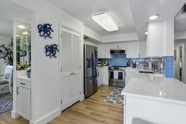 kitchen featuring stainless steel appliances, tasteful backsplash, visible vents, white cabinets, and light wood-type flooring