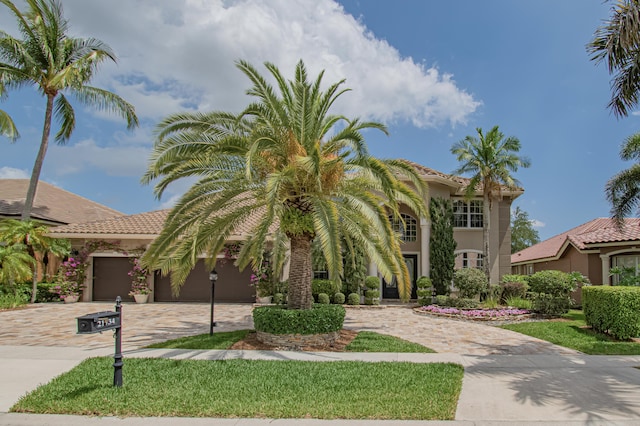 mediterranean / spanish-style house with an attached garage, stucco siding, a tile roof, and decorative driveway