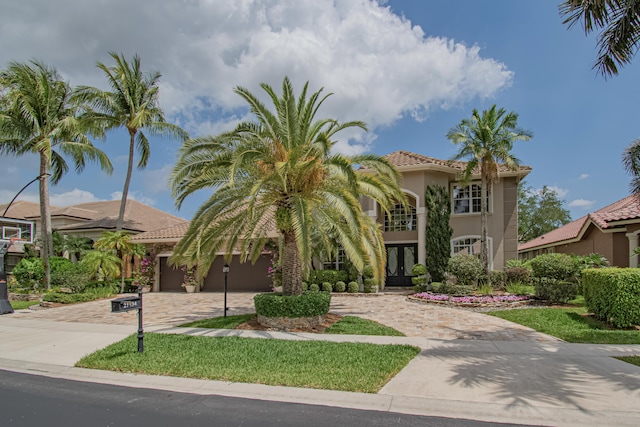 mediterranean / spanish-style house featuring stucco siding, decorative driveway, a tile roof, french doors, and a garage
