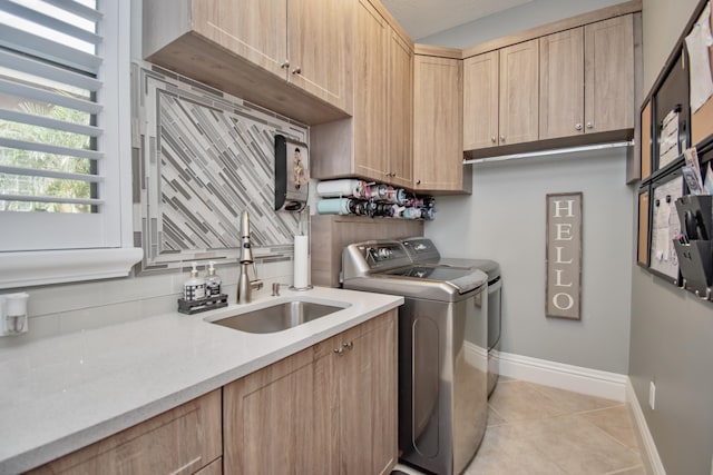 laundry room with baseboards, light tile patterned floors, washing machine and clothes dryer, cabinet space, and a sink