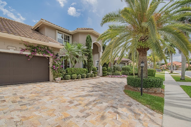 mediterranean / spanish-style home with a garage, stucco siding, a tile roof, and decorative driveway