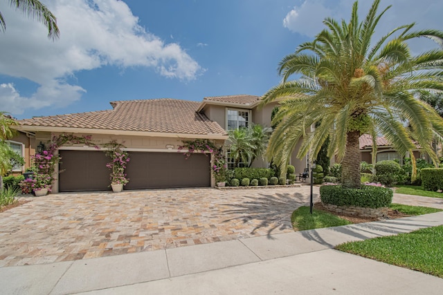 view of front facade with an attached garage, stucco siding, a tile roof, and decorative driveway