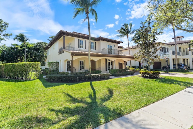 mediterranean / spanish-style house with a tile roof, stucco siding, a front yard, a balcony, and driveway